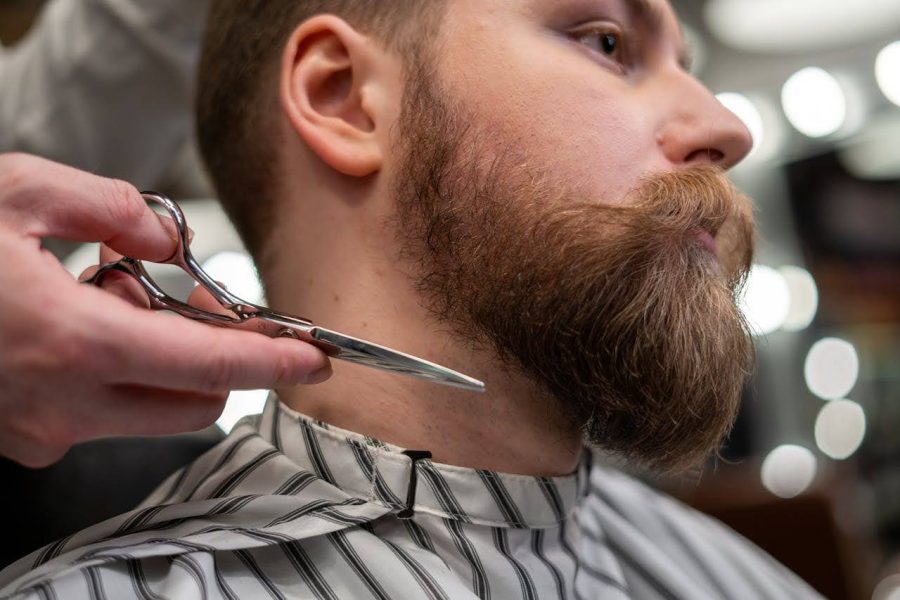  Barbiere che regola la barba di un cliente con le forbici
